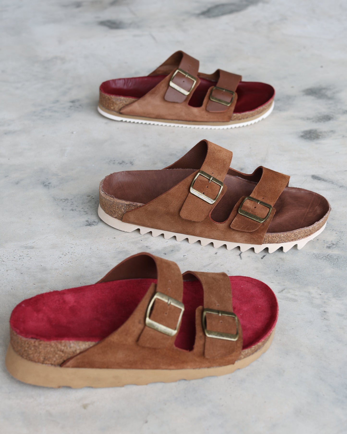 Pair of brown and red sandals with buckles on a marble surface