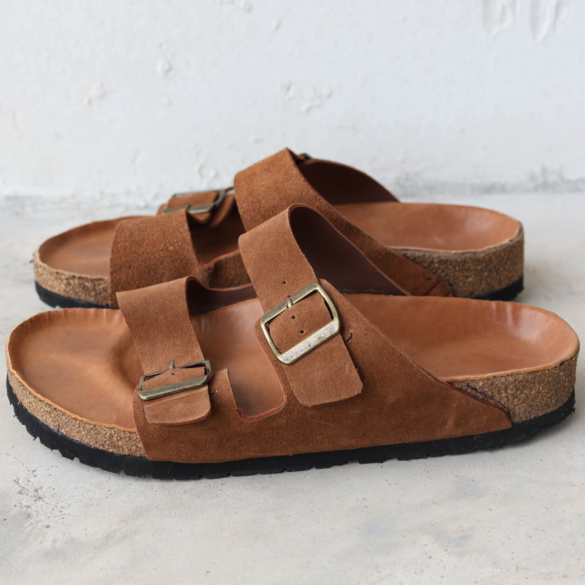 Pair of brown sandals with buckles on a light gray surface